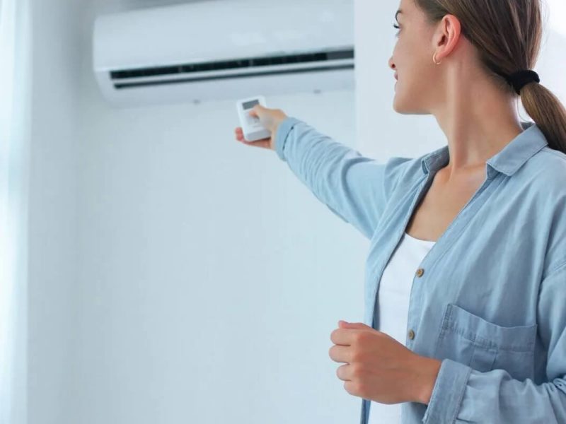young-woman-adjusts-temperature-air-conditioner-using-remote-control-room-home